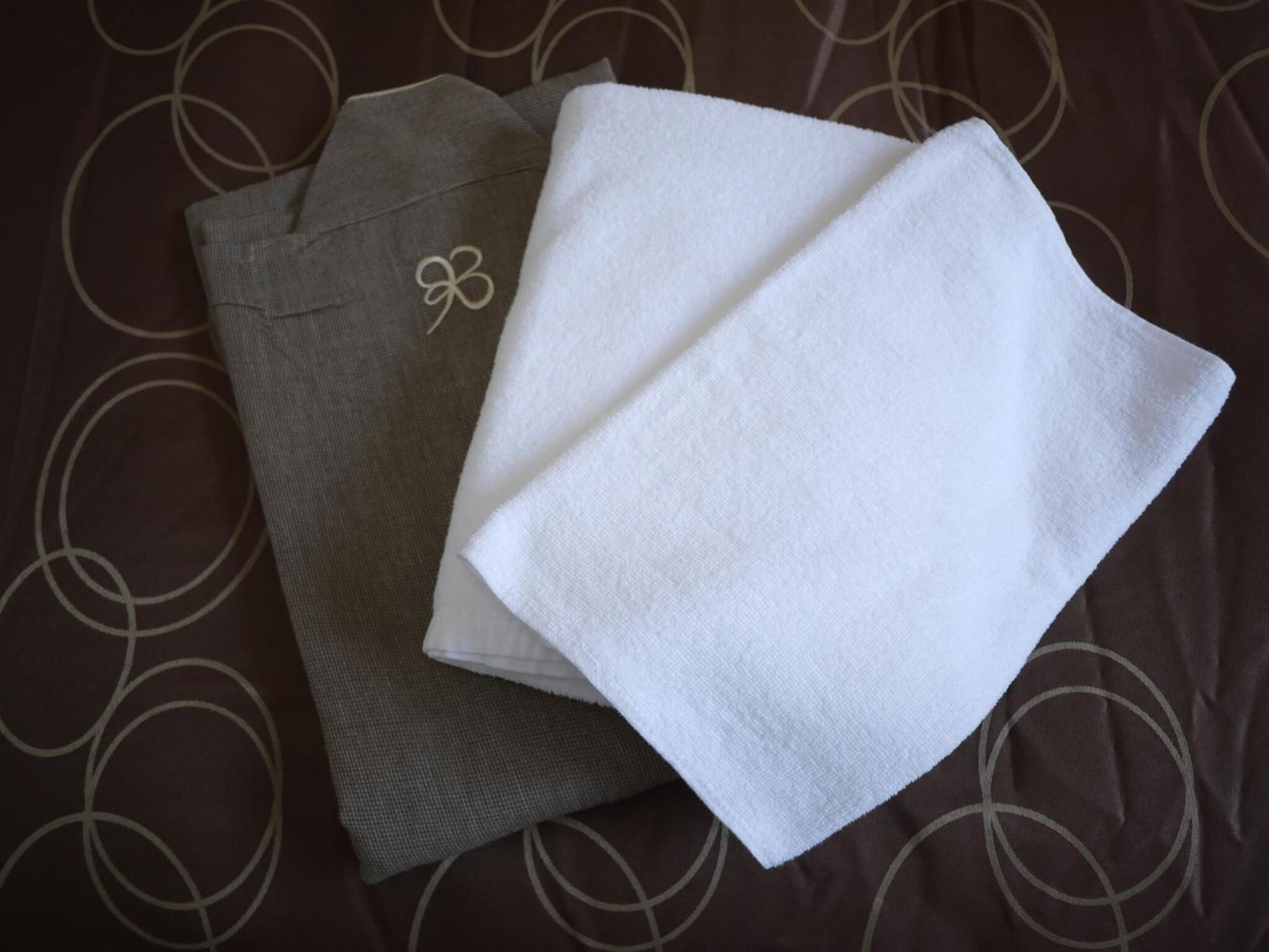 Two folded towels, one white and one gray, on a brown fabric with circular patterns.