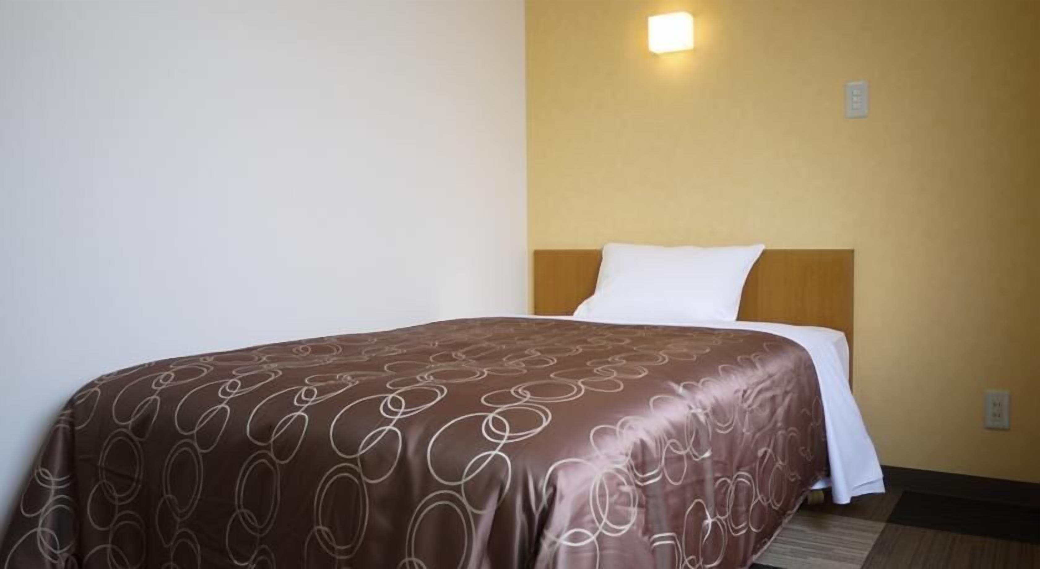 Habitació d'hotel amb un llit, un capçal, una làmpada penjada a la paret i una presa elèctrica.