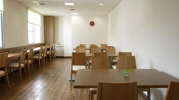 A spacious room with multiple wooden tables and chairs, large windows, and a clock on the wall.