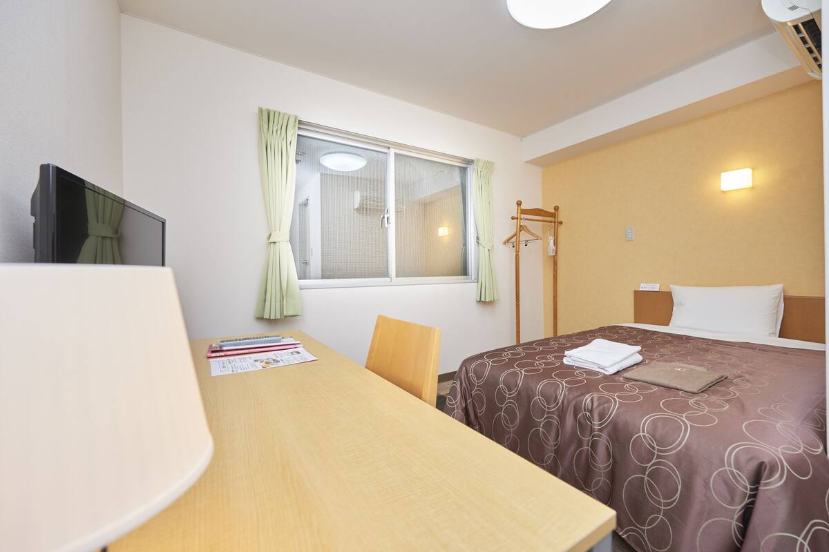 A hotel room with a bed, a desk, a chair, a TV, and a window with curtains.