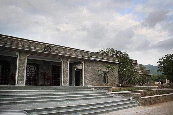 A building with a stone facade, a set of stairs leading to the entrance, and a clear sky. - King's Abode (Kumbhalgarh)
