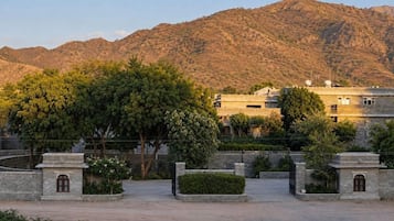 A courtyard with a stone wall, a tree, and a building with multiple windows and a flat roof.