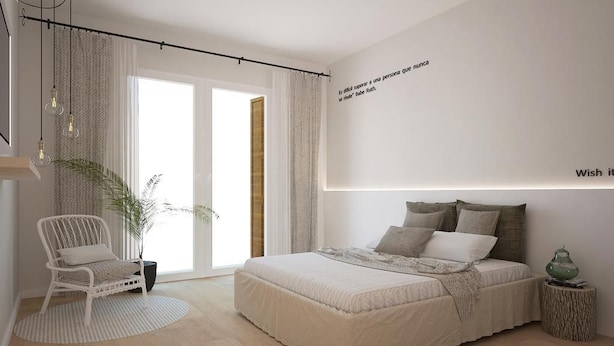 A bedroom with a bed, a chair, a plant, and a bedside table.