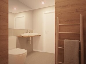A modern bathroom with a toilet, sink, mirror, and wooden towel rack. - Dynamic Hotels Caldetes Barcelona (Arenys de Munt)