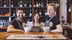 Un bar avec trois personnes derrière le comptoir, une variété de bouteilles exposées sur des étagères et une enseigne indiquant « HOLGATE ».