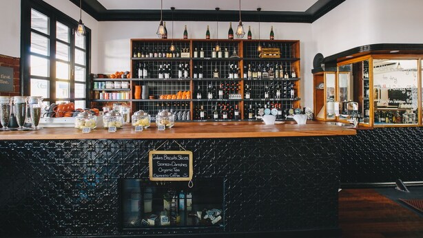 Un espace bar avec des étagères remplies de bouteilles, un panneau indiquant les boissons disponibles et un mur noir à texture.