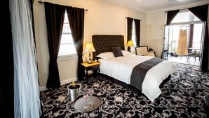 Une chambre d’hôtel avec un grand lit, deux lampes de chevet, une petite table avec une bouteille et des verres, et une vue sur l’extérieur par une porte.