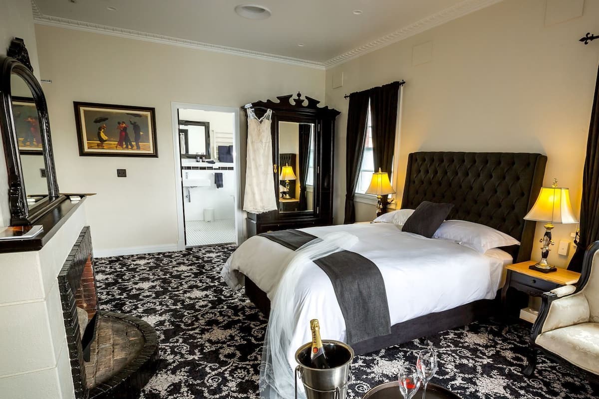 A hotel room with a large bed, two bedside lamps, a chair, a mirror, and a painting on the wall.
