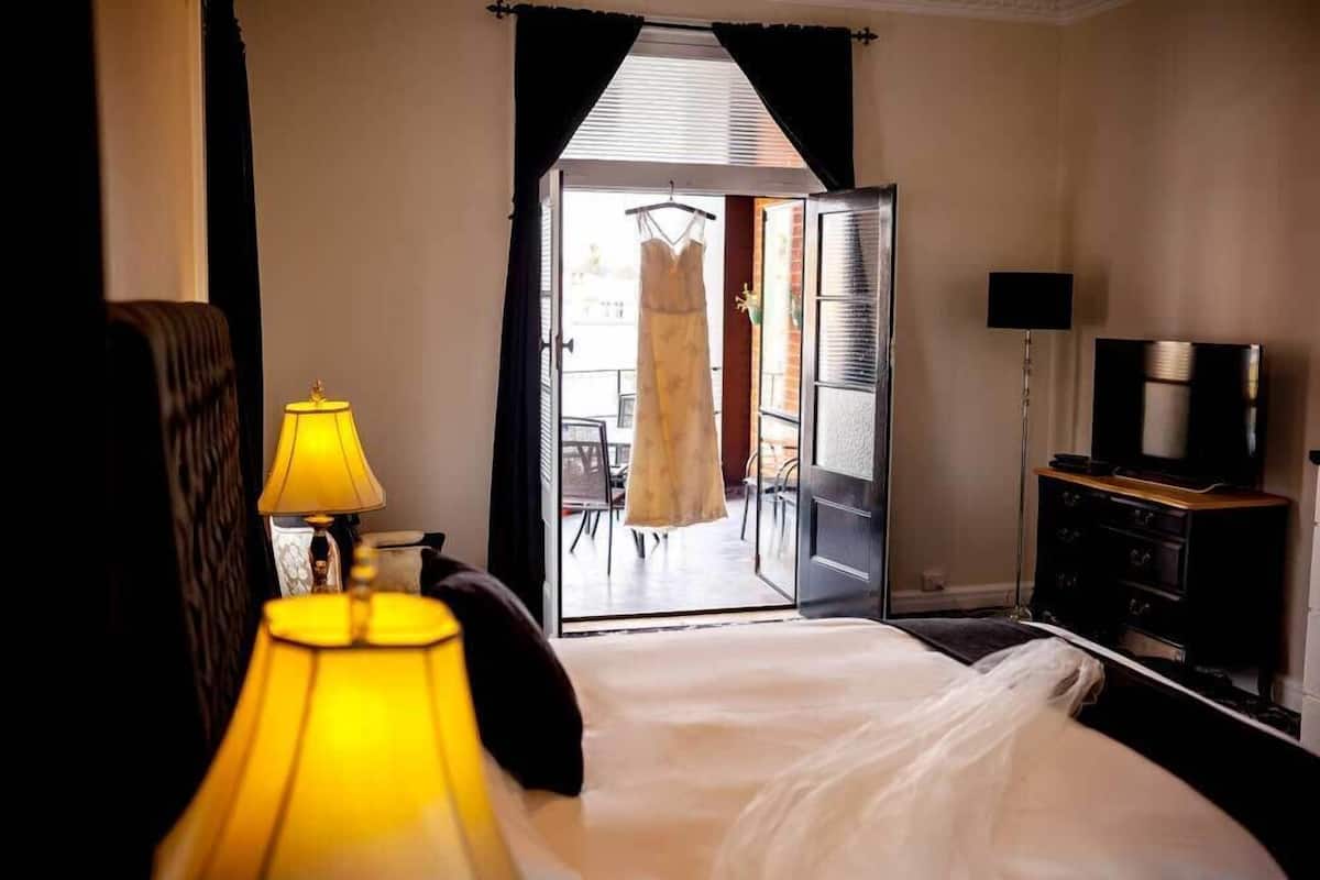 A hotel room with a bed, a lamp, a TV, and a view of an outdoor area with a dress on a hanger.