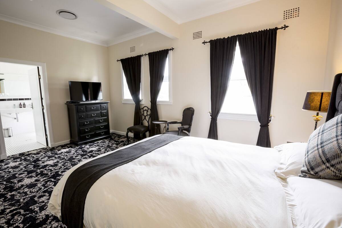 A hotel room with a large bed, a dresser, a TV, a desk, and two chairs.