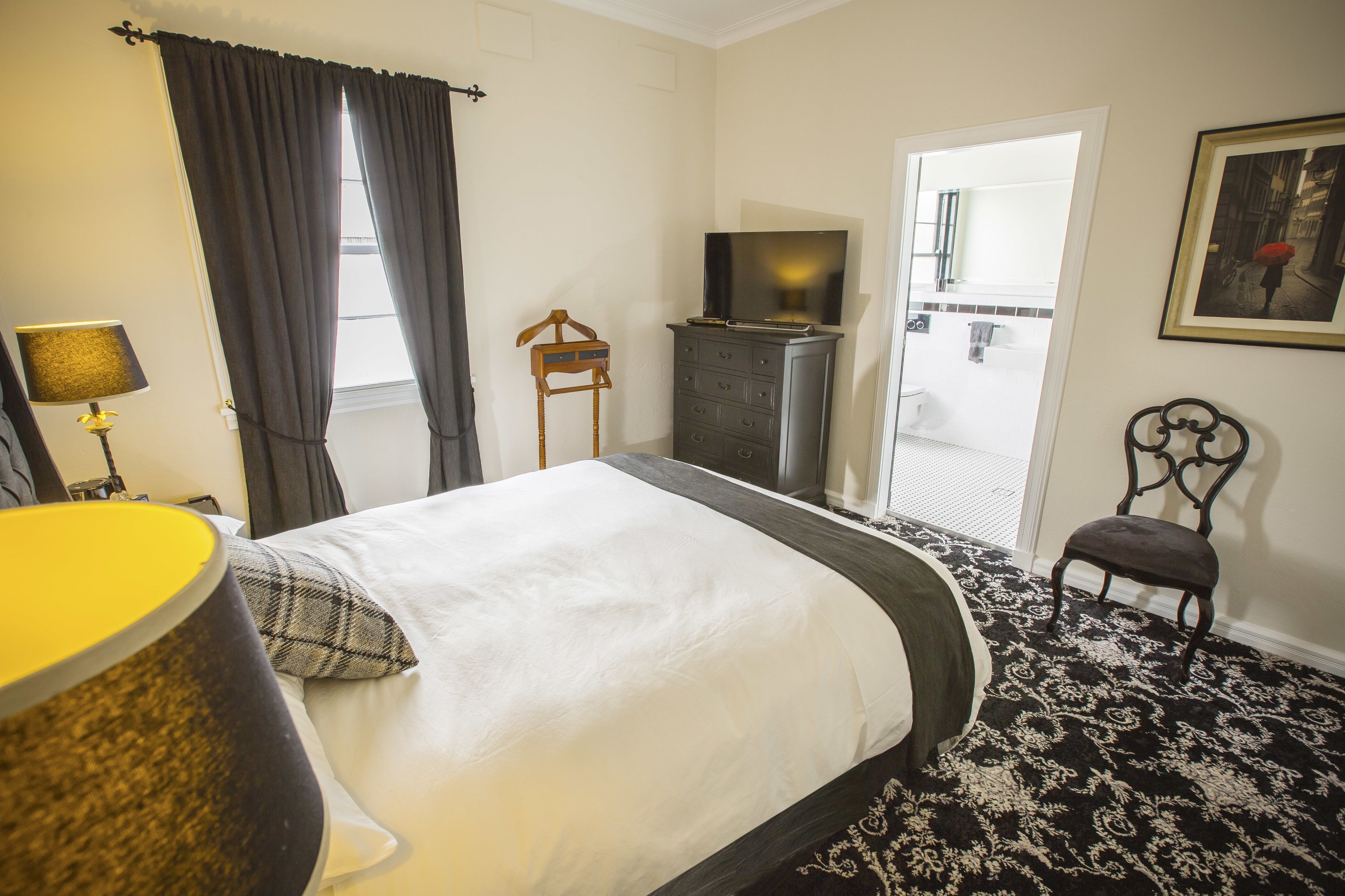 A hotel room with a bed, a dresser, a television, a chair, and a door leading to a bathroom.