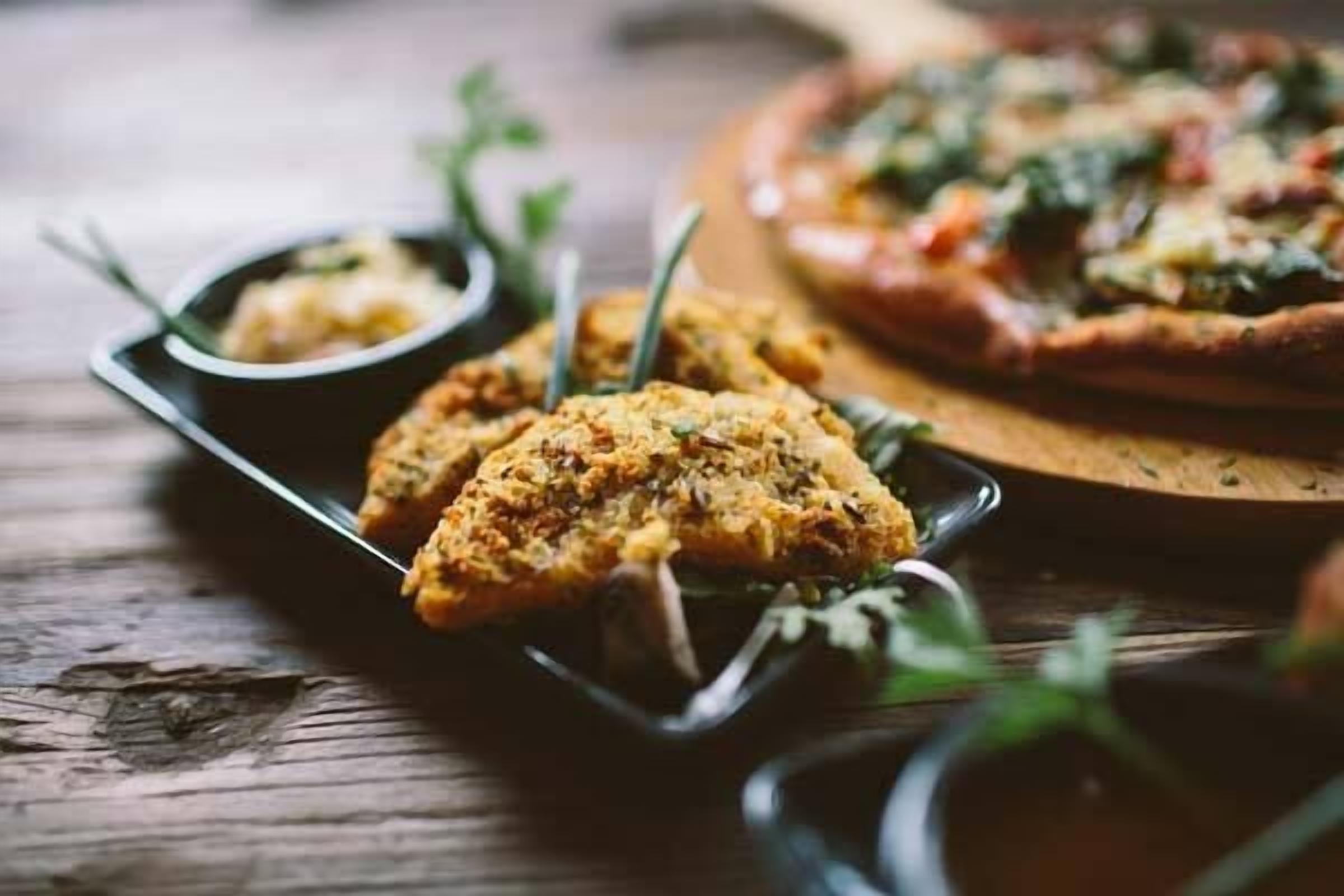 A wooden table with a pizza and a dish of food.