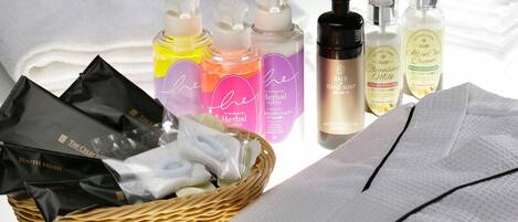 A collection of personal care items including bottles of hand soap, a facial cleanser, and a cream, along with a basket containing a toothbrush and a bag of cotton pads.