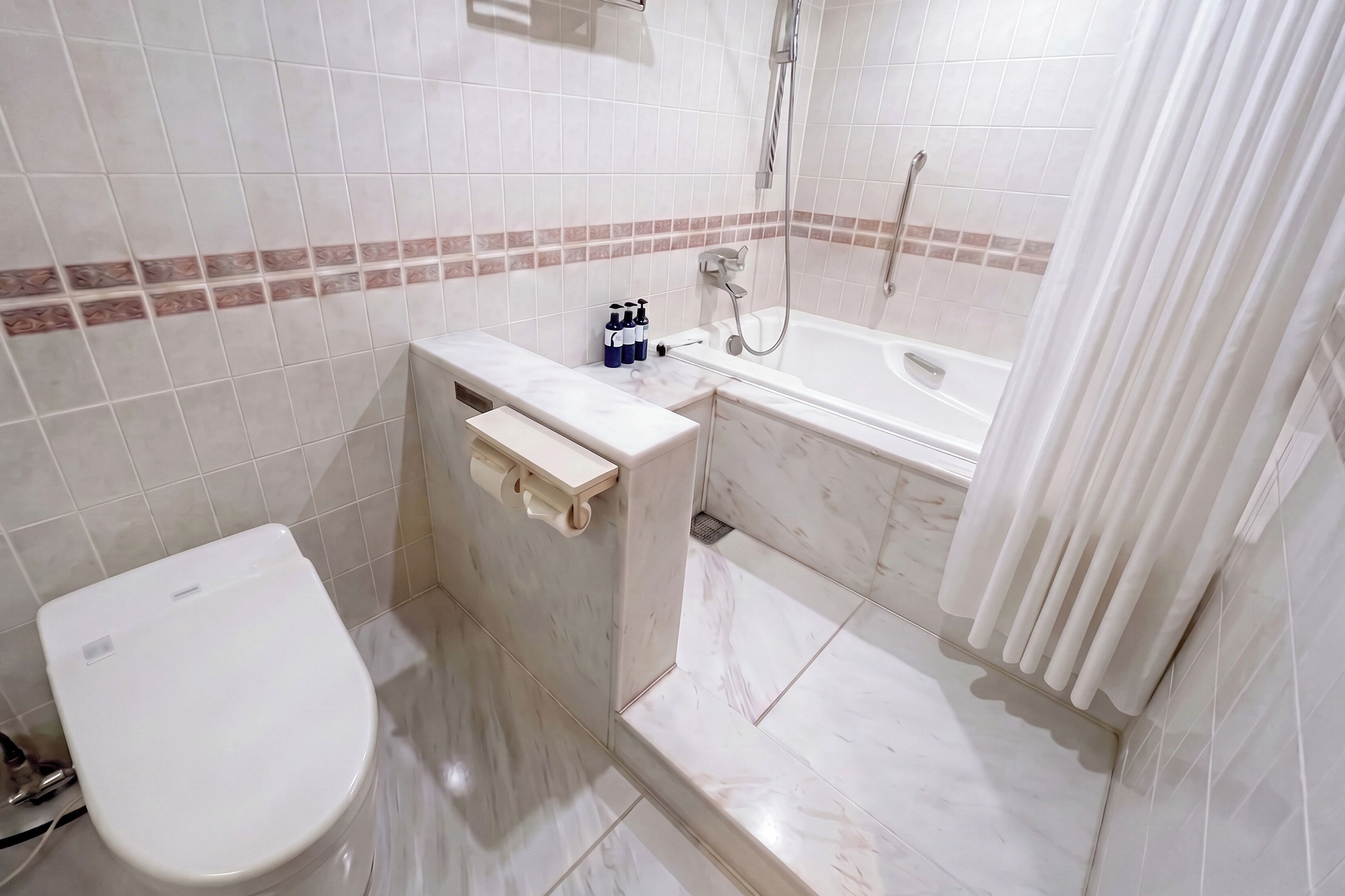 A bathroom with a toilet, a sink with toiletries, and a bathtub with a showerhead.