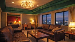 A hotel room with a leather sofa set, a wooden coffee table, a chandelier, and a city view through large windows. - The Celecton Fukushima (Fukushima)