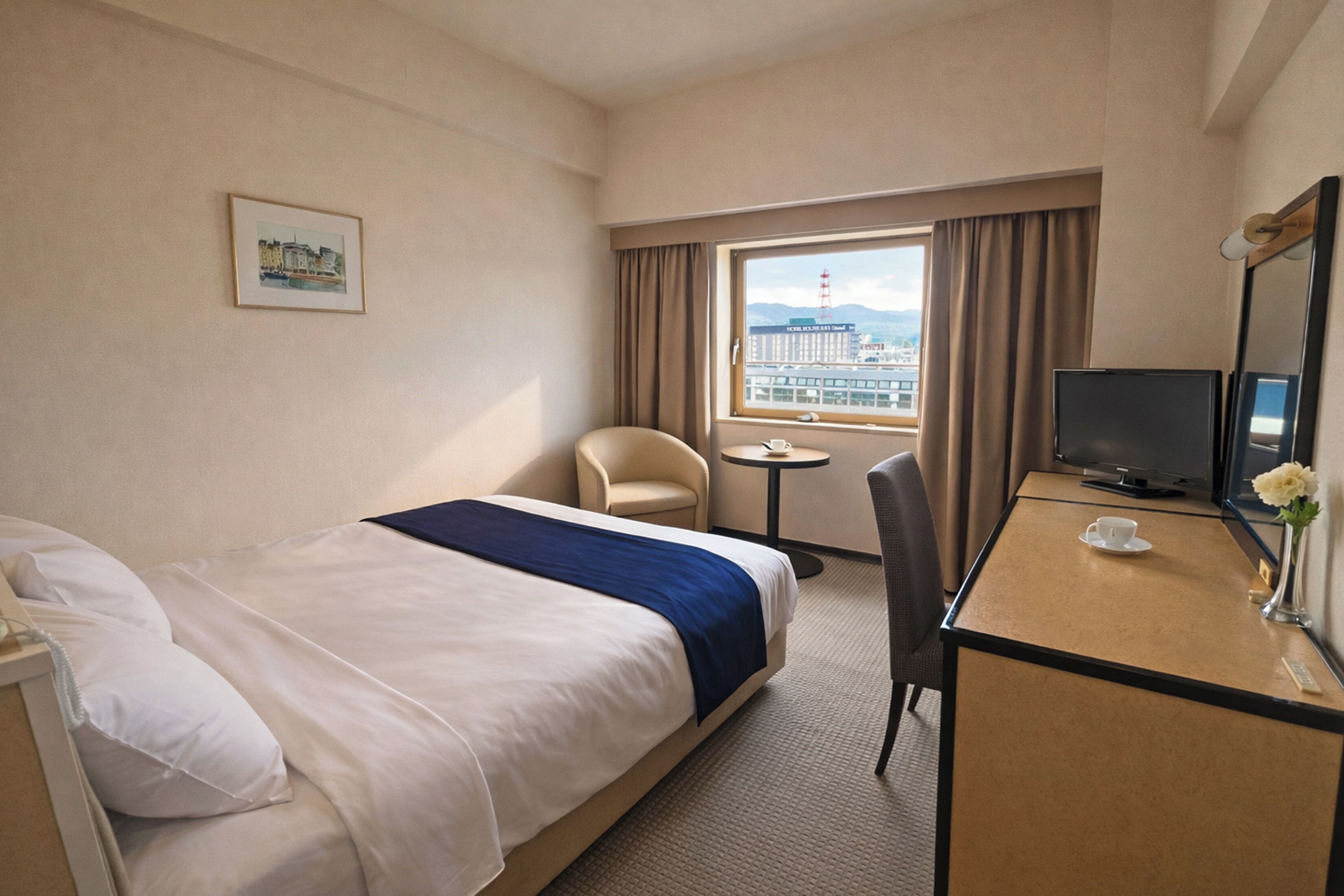 A hotel room with a bed, a desk, a chair, a television, and a window with a view of a building.
