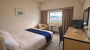 A hotel room with a bed, a desk, a chair, a television, and a window with a view of a building.