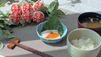 Una mesa con un tazón de arroz, una taza de té y objetos decorativos, incluyendo envoltorios rojos y blancos y hojas verdes.