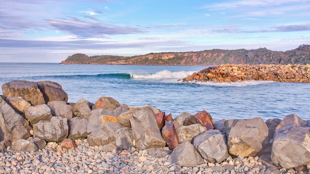 Una costa rocosa con olas rompiendo contra las rocas y una vista distante de un paisaje montañoso.