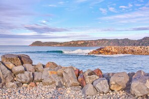 A rocky shoreline with waves crashing against the rocks and a distant view of a hilly landscape. - North Haven Holiday Village (North Haven)