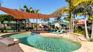 Una piscina con agua cristalina, rodeada de palmeras y una zona con sombra.