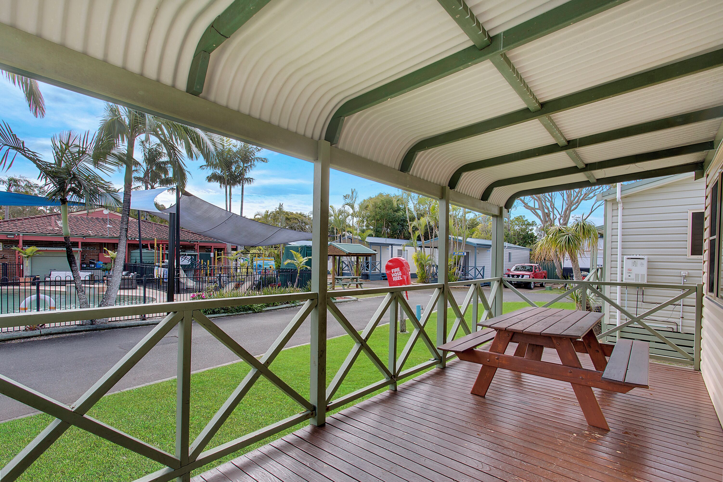 A covered outdoor area with a picnic table and a view of a street with buildings and palm trees.