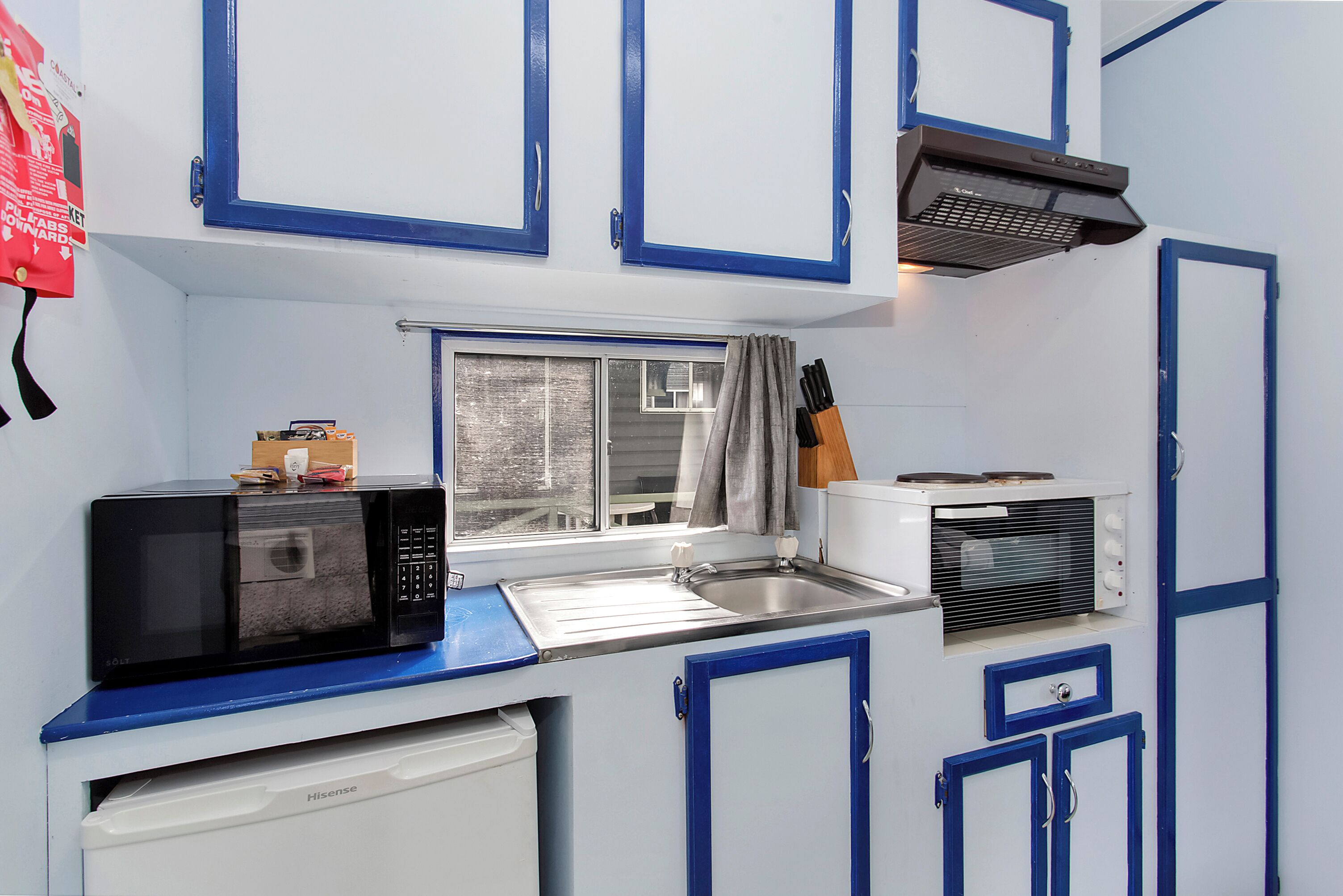 A compact kitchenette with a microwave, stove, sink, and cabinets.