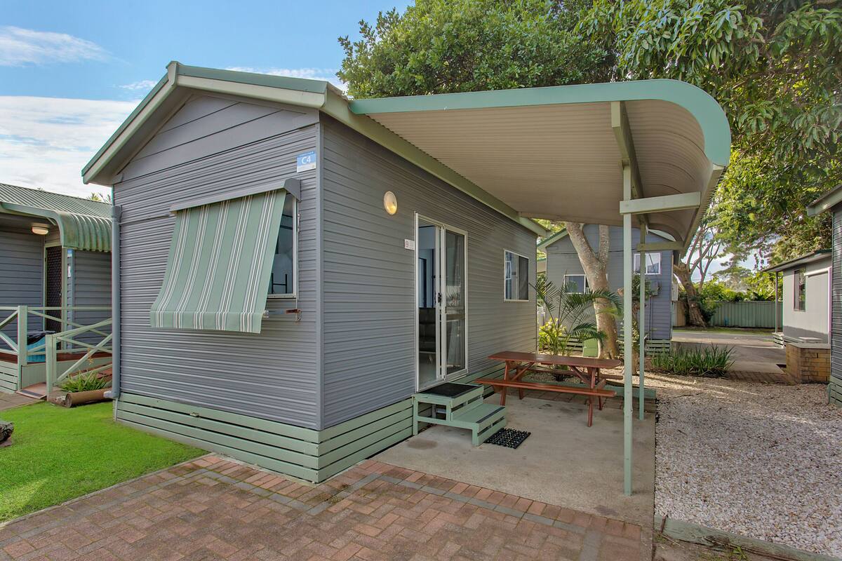 A single-story mobile home with a covered patio area, a small outdoor seating area, and a well-maintained lawn.
