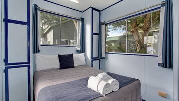 A room with a bed, two windows, and a view of a tree.
