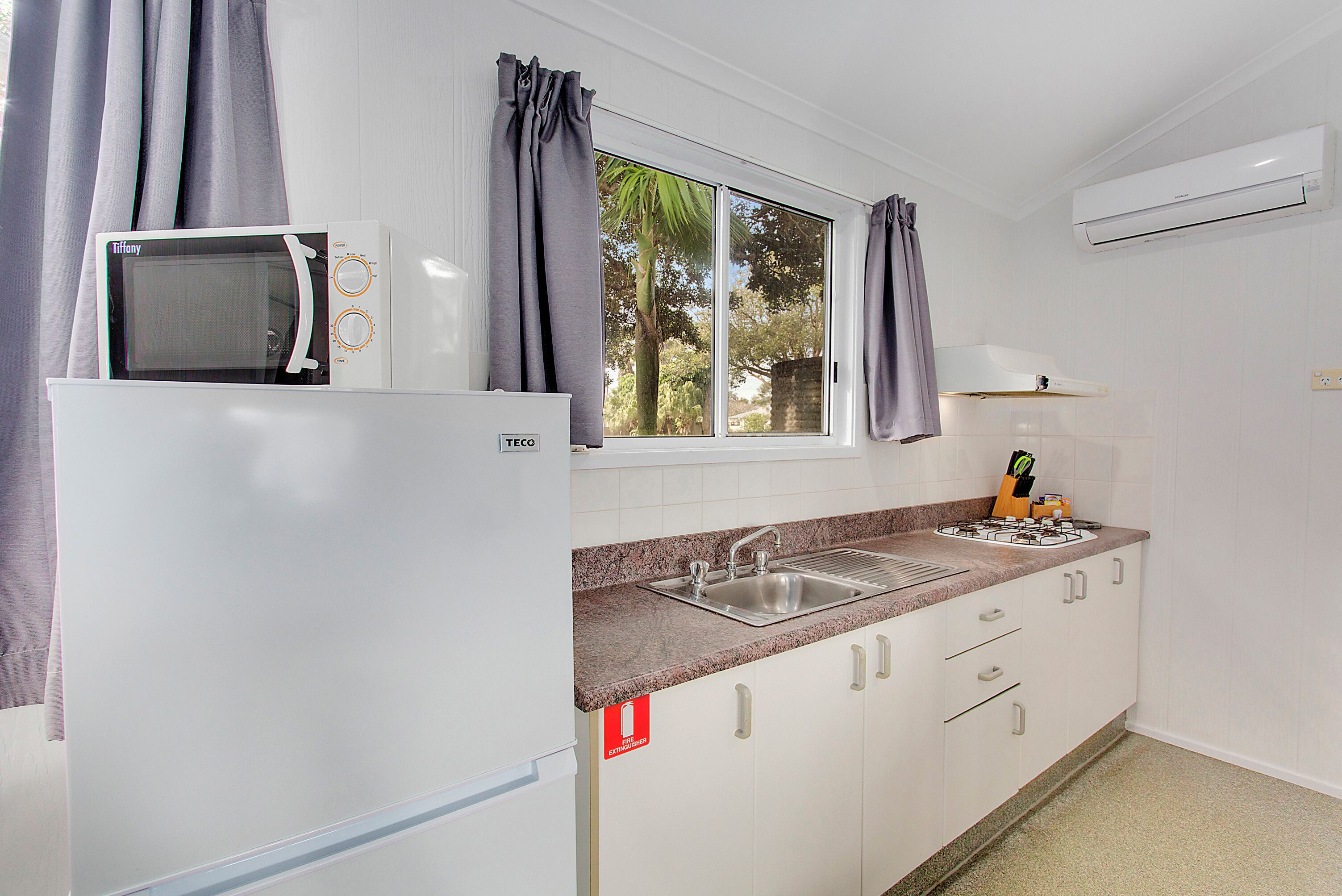 A kitchen with a white refrigerator, a microwave, a sink, and a window with curtains.