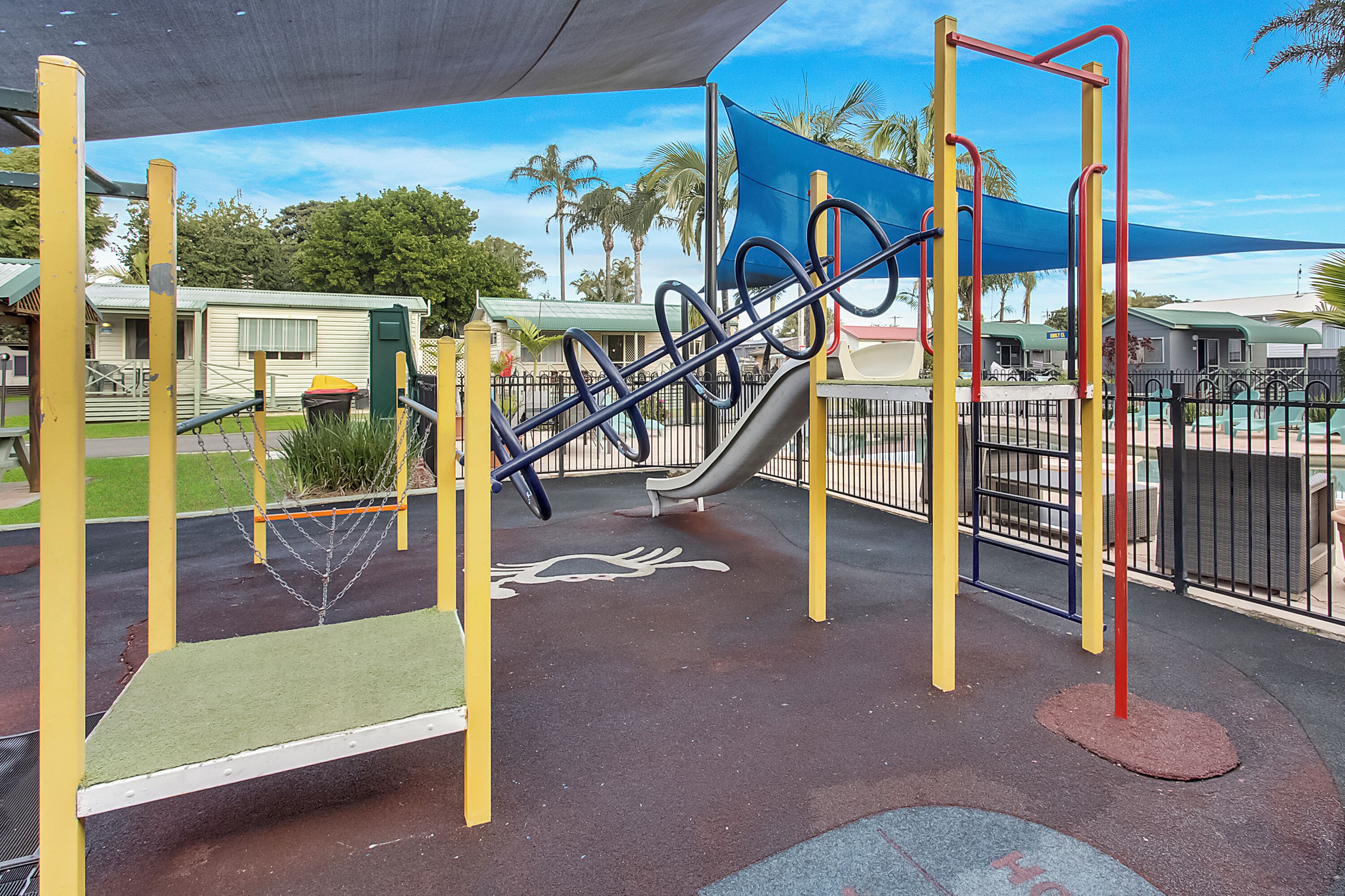 Un parque infantil con tobogán, estructuras para escalar y una zona con sombra.