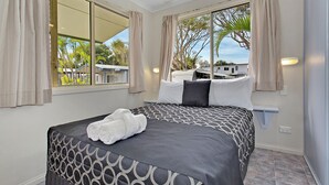 Un dormitorio con una cama grande, una ventana con cortinas y vistas a palmeras y casas.