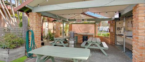 An outdoor patio area with picnic tables, a barbecue grill, and a covered seating area.