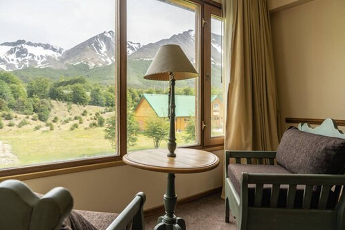 Ein Zimmer mit Blick auf Berge und eine grüne Landschaft. Es steht ein runder Tisch mit einer Lampe und einem Stuhl darin.