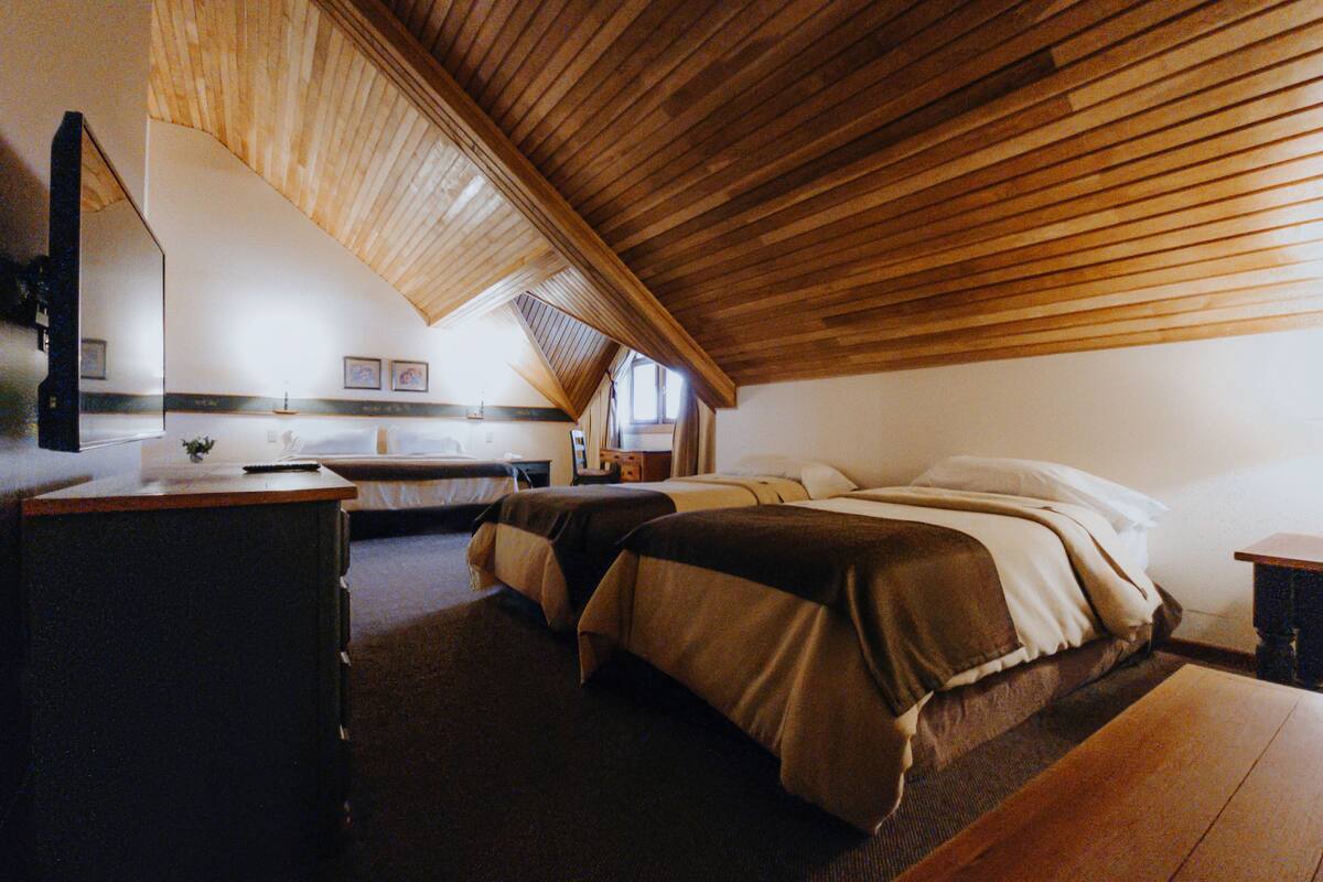 Ein Zimmer mit schrägen Wänden, einem Bett mit zwei Kissen, einem Nachttisch und einem Spiegel.