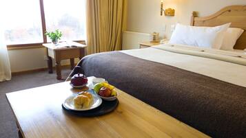 Habitación de hotel con una cama bien hecha, una mesita de noche con una bandeja de artículos de desayuno, una lámpara y una ventana con cortinas.