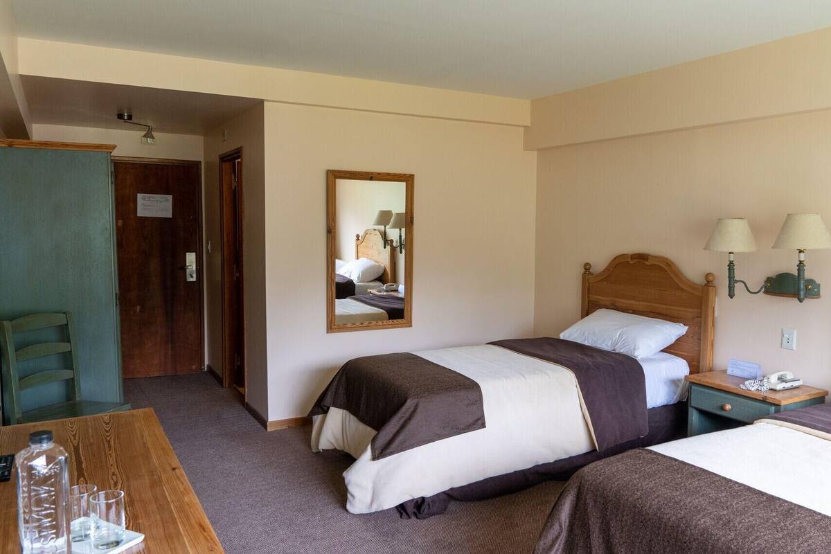 Ein Hotelzimmer mit zwei Betten, einem Schreibtisch mit Lampe, einem Spiegel und einem Kleiderschrank.