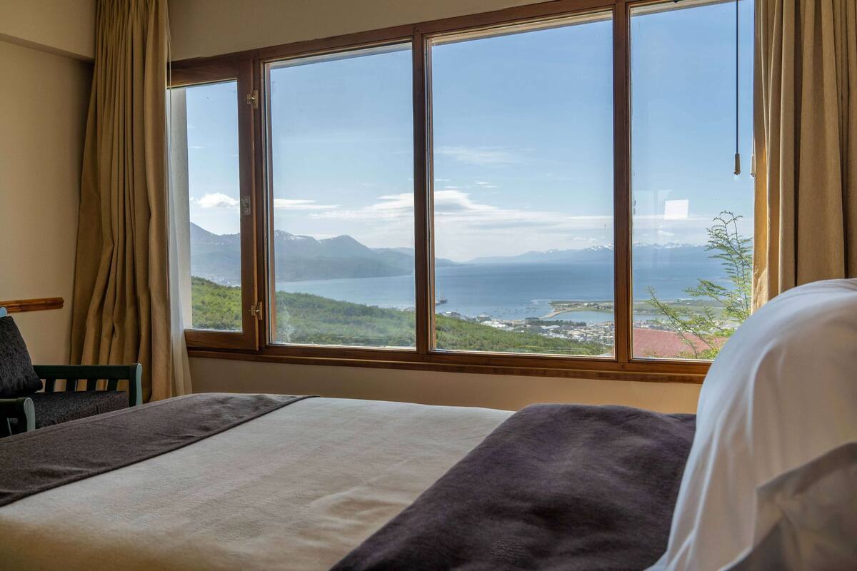Ein Hotelzimmer mit großem Fenster und Blick auf eine Küstenlandschaft, einschließlich Bergen und einem Gewässer.