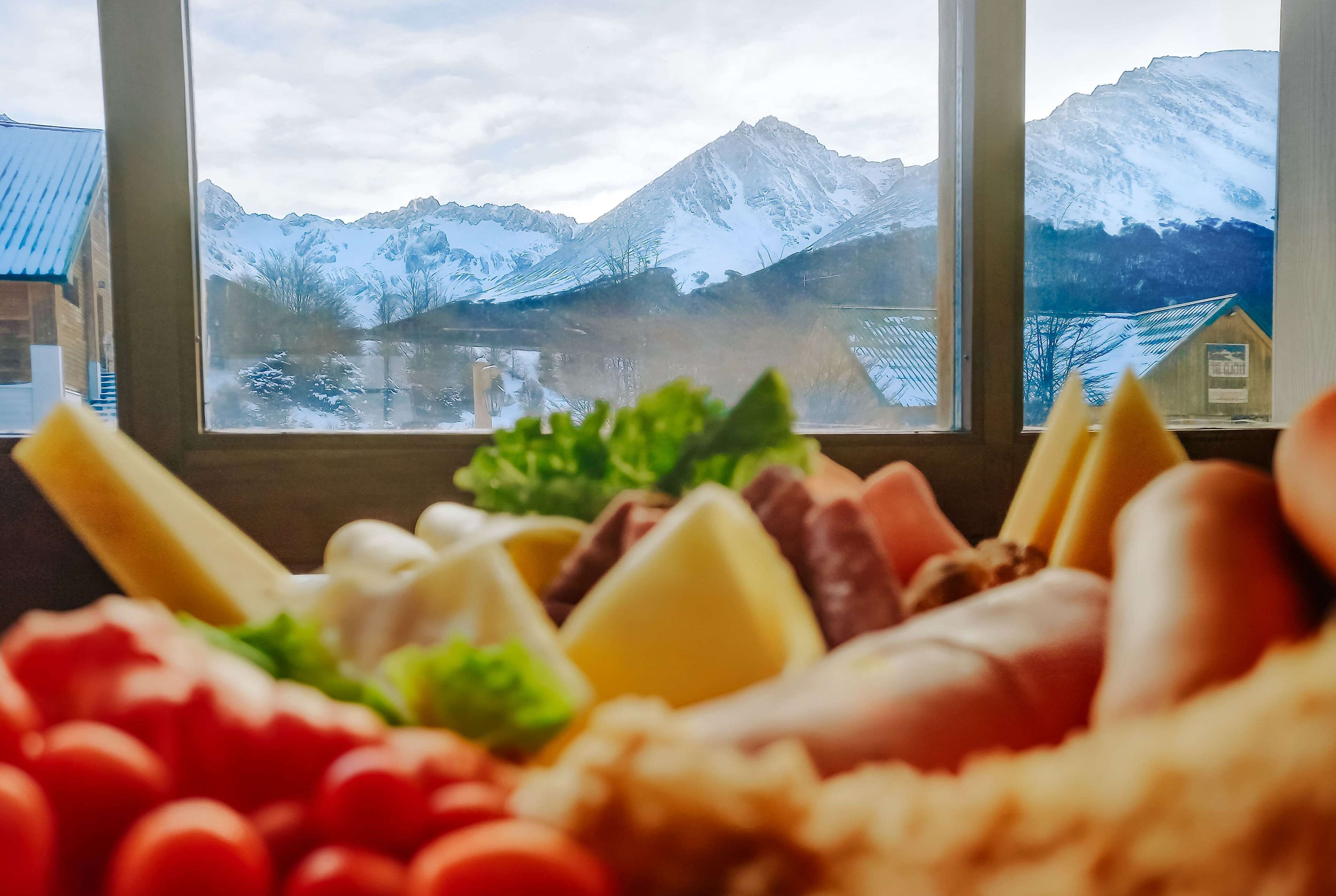 A mountain view through a window with a cheese platter in the foreground.
