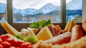 A mountain view through a window with a cheese platter in the foreground.