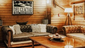A cozy hotel room with a leather sofa, a wooden coffee table with a plate of pastries, and a sign reading "HOTEL DEL GLACIER USHUJAIA - PATAGONIA ARGENTINA".