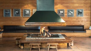 A wood-paneled room with a large fireplace, framed pictures on the wall, and a black leather couch.