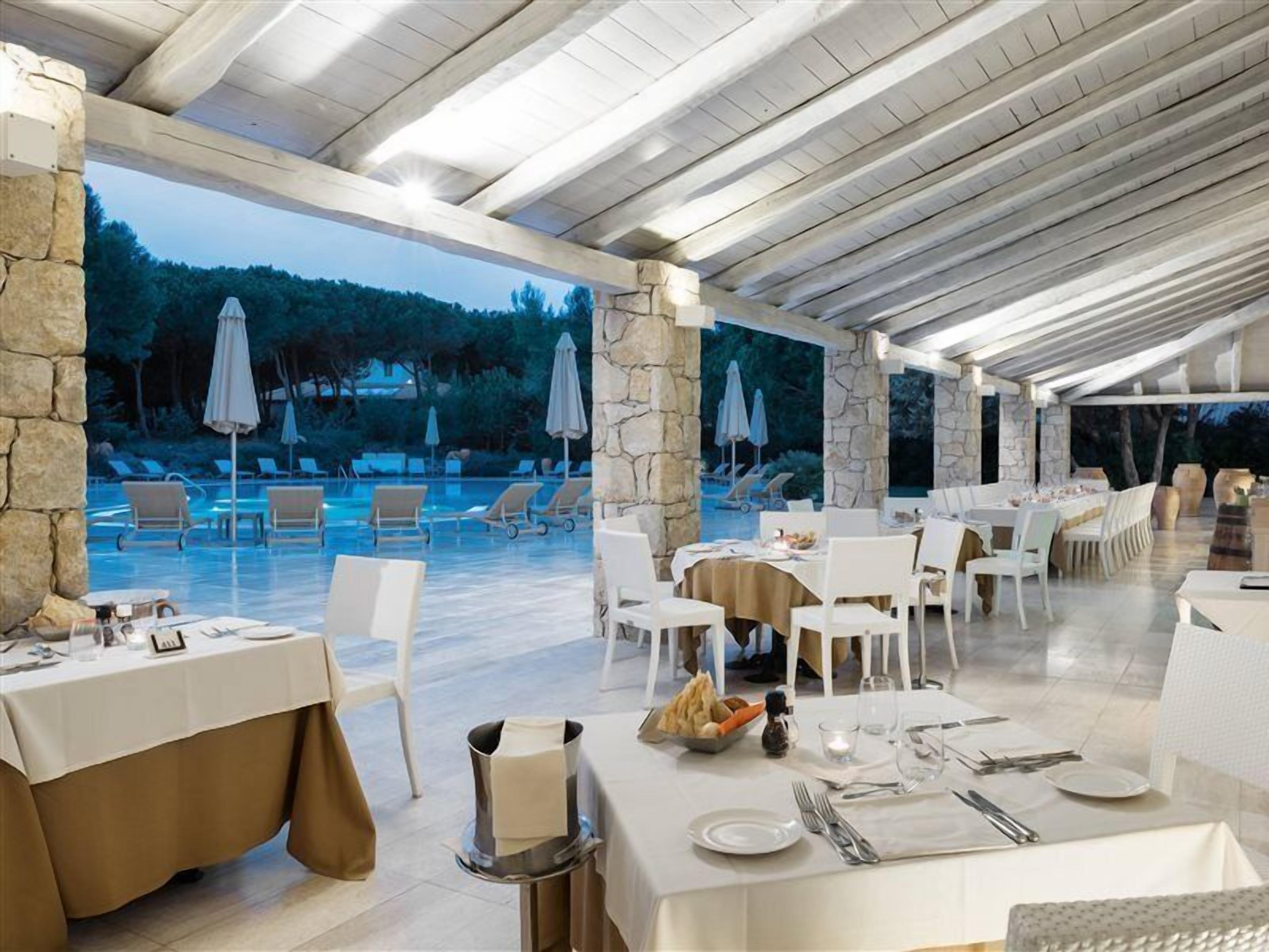 Ein Restaurant mit Außenbereich, das auf einen Pool mit Blick auf Bäume und Steinsäulen blickt.