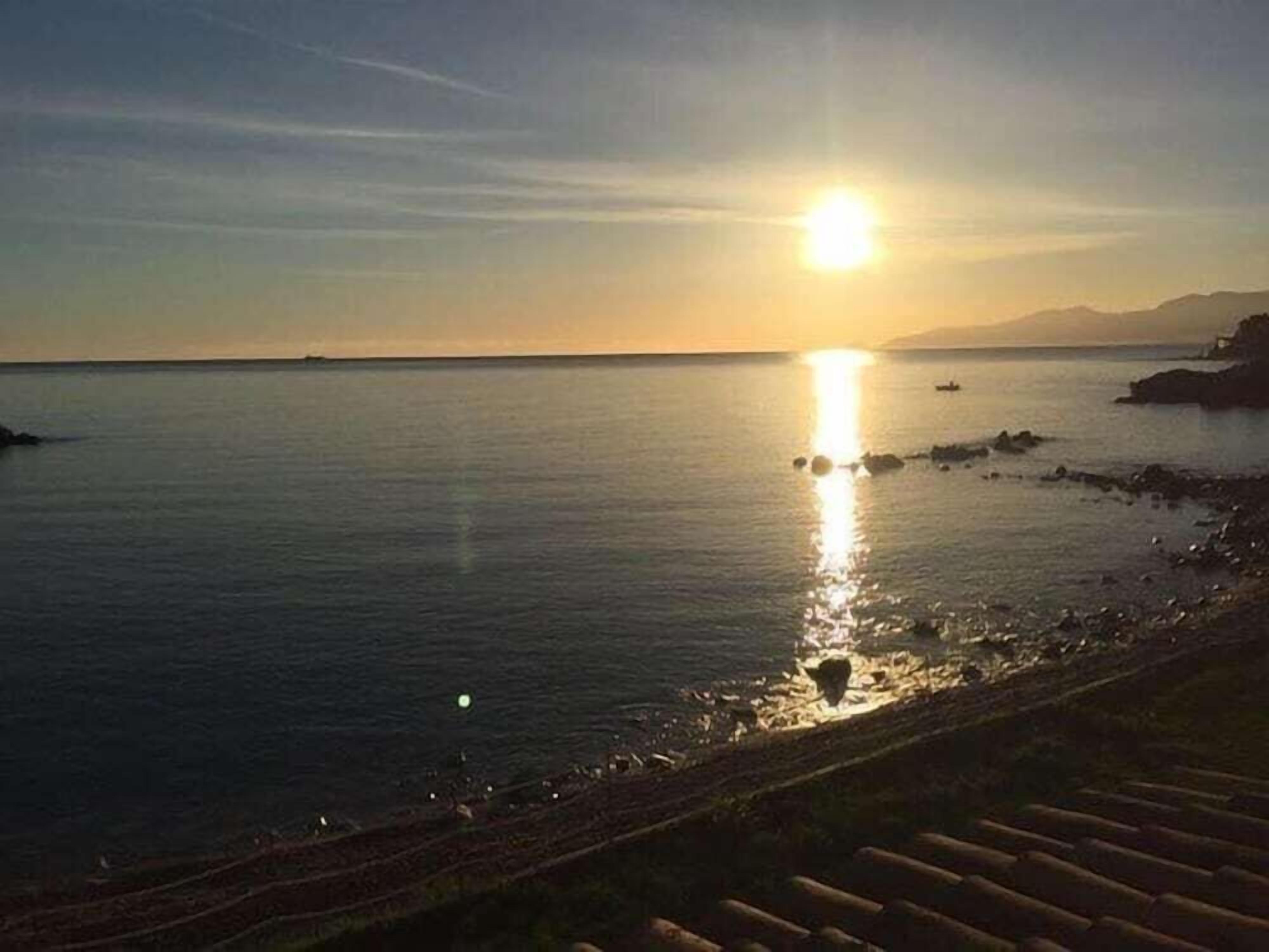 A sunset over a calm sea with a rocky shoreline and a wooden walkway.