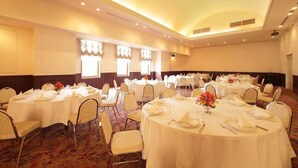 Une salle de banquet avec des tables rondes disposées en rangées, prêtes pour le repas, et des chaises autour de chaque table.