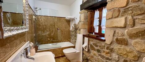 A bathroom with a stone wall, a bathtub, a toilet, and a sink.