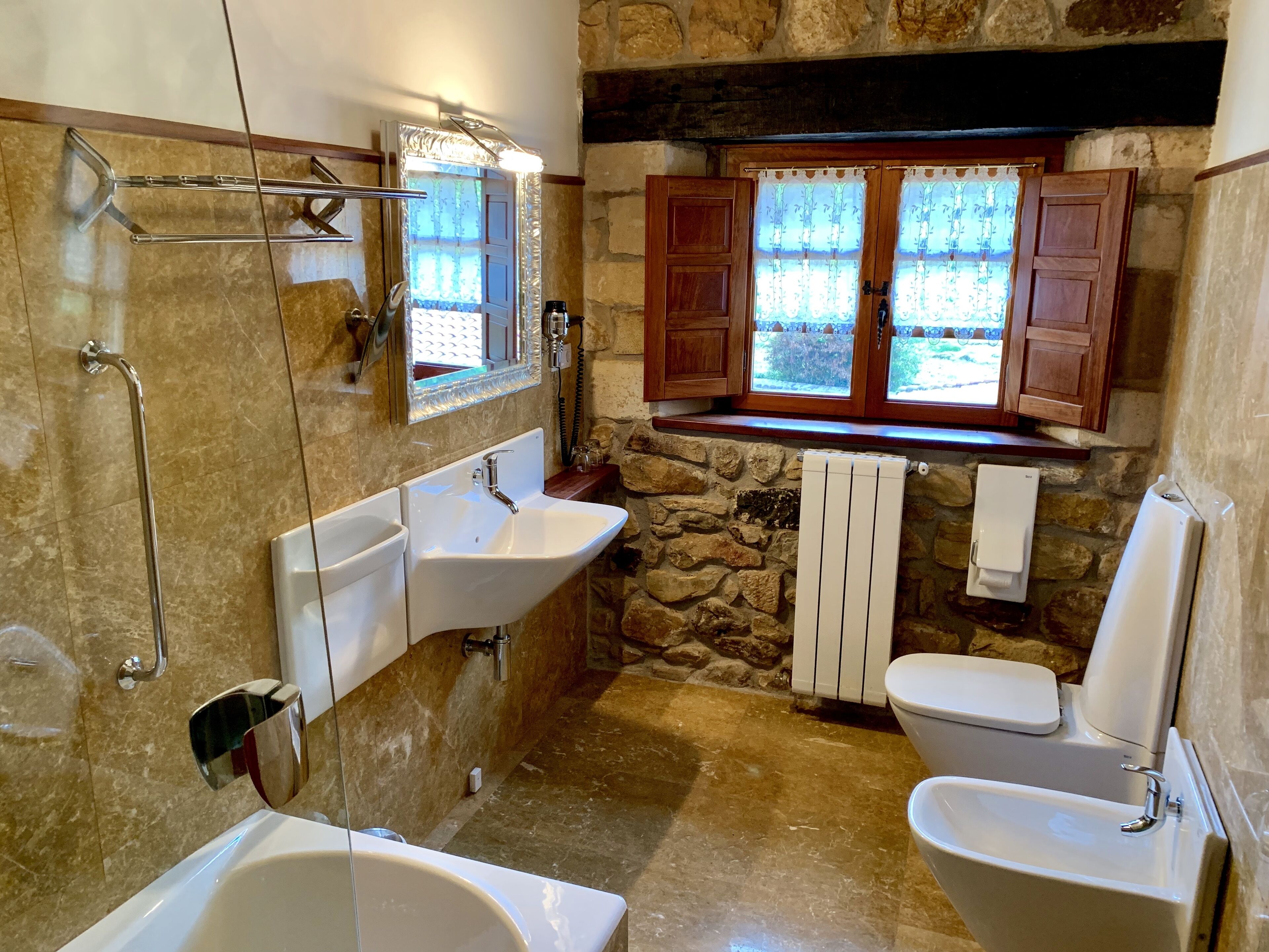 Un baño con bañera, dos lavabos, inodoro, ducha y ventana con cortinas.