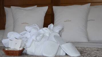 Quarto de hotel com cama, almofadas brancas, roupão, chinelos e um cesto com produtos de higiene pessoal.