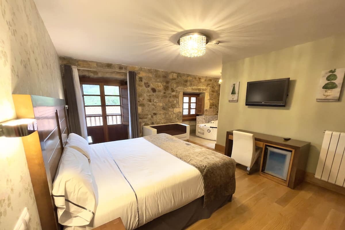 Een hotelkamer met een groot bed, een bureau, een televisie, een stenen muur en een raam met uitzicht.