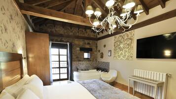 A bedroom with a large bed, a stone wall, a modern bathroom, and a chandelier.
